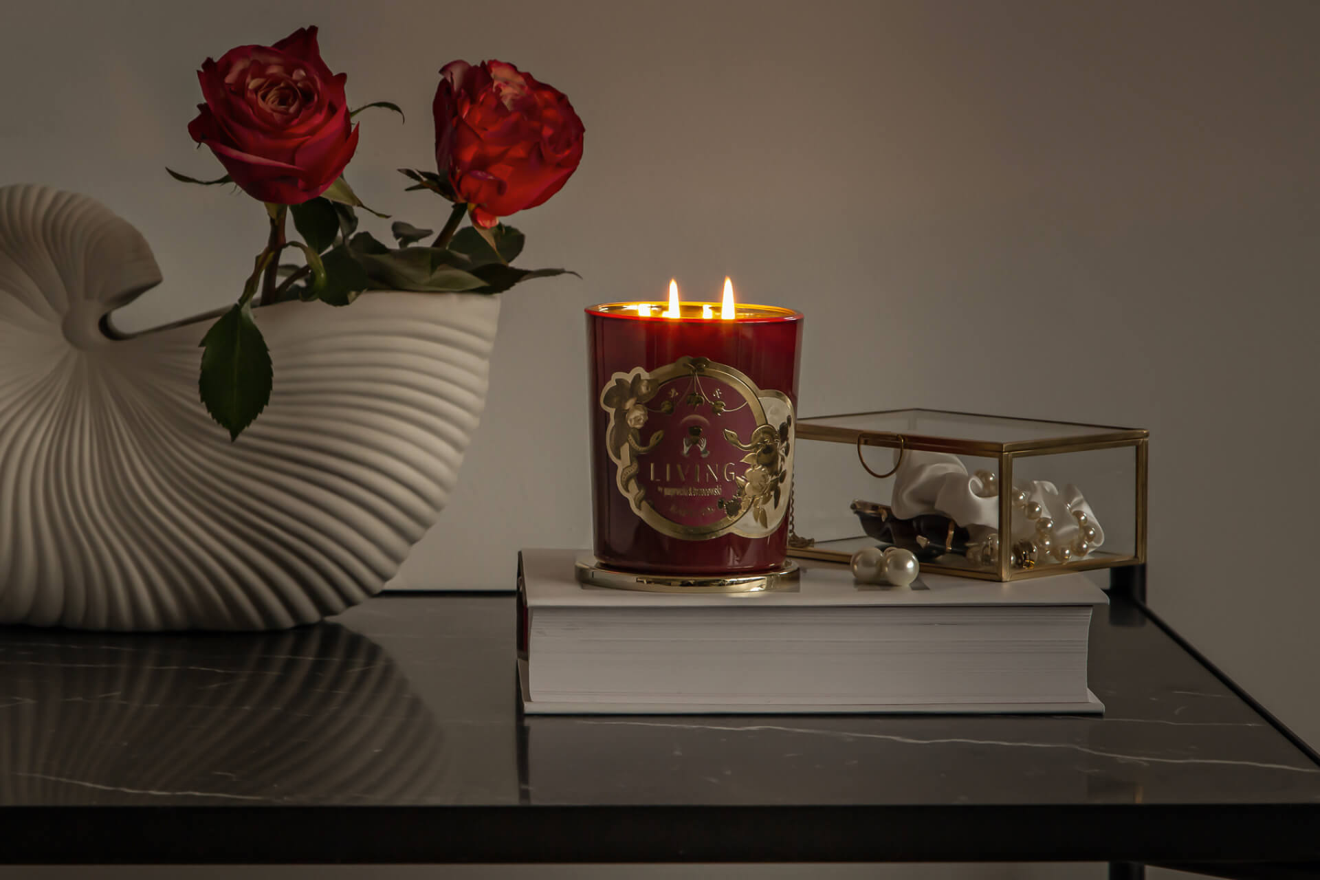 bordowa świec Rapture pomiędzy szkatułka z biżuterią a wazonem z czerwonymi różami